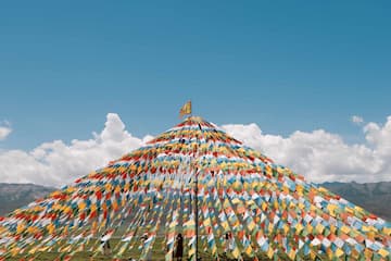 山顶堆满彩色经幡在蓝天白云下飘扬远山连绵