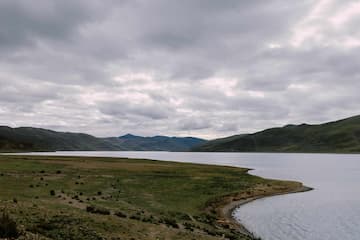 图片展示了湖泊、草地和山脉的自然景观，天空阴云密布。