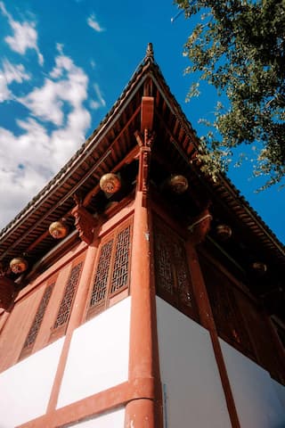 仰视拍摄的中式建筑一角，红白墙体，飞檐翘角，悬挂灯笼，背景是蓝天白云。