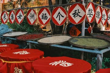图片展示了挂着圆形匾额和摆放着红色盖子容器的场景，容器里有谷物晾晒。