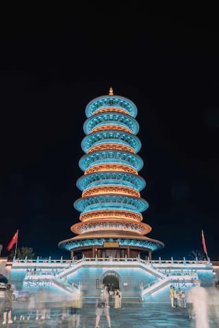 图片展示了一座在夜间被灯光照亮的宝塔，建筑结构层次分明，周围有台阶和人群。