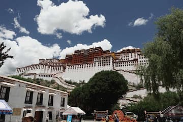 图片展示了在蓝天白云映衬下的布达拉宫建筑群，宫殿位于远处山顶上。