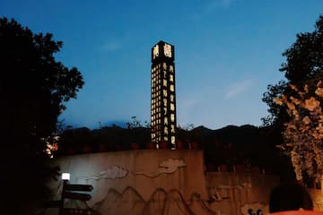 图片展示了一座高塔在夜幕下的景象，塔身有发光的文字，背景是山脉，下方有墙绘装饰。
