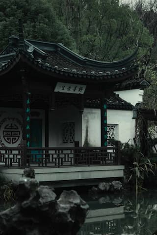 图片展示了一座中式建筑，它临水而建，周围环绕着茂密的树木，营造出一种宁静而古朴的氛围