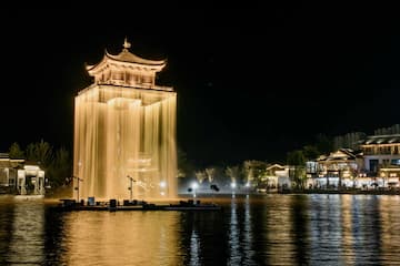 夜间，湖面上有一座被灯光照亮的古塔，塔身被水幕环绕。