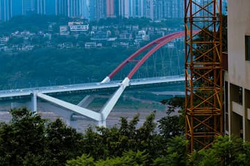 红色拱桥横跨江面城市建筑群在远处树木在前景