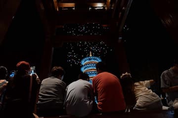 一群人正在观看夜间灯光秀，塔身被照亮，夜空中闪烁着光点。