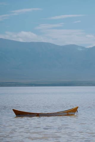平静的湖面上漂浮着一艘小船远处的山脉在薄雾中若隐若现
