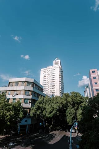 图片展示了城市中的建筑群，包括高层建筑和多层建筑，天空湛蓝，有少量白云，街道两旁绿树成荫。