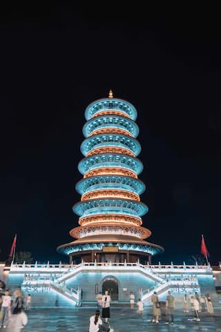 图片展示了一座多层宝塔建筑，在夜间被灯光照亮，底部有台阶和人群。