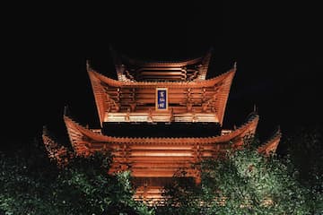 夜间拍摄的木制多层塔楼，被灯光照亮，底部有树木。