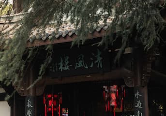 建筑屋檐下悬挂着红灯笼 牌匾上写着文字 树枝遮盖部分屋檐