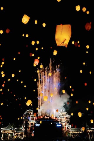 夜空中，许多天灯漂浮，建筑上方有烟花绽放。