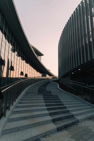 一张从低角度拍摄的室外照片，展示了连接两栋现代建筑的阶梯，其中一栋建筑有玻璃幕墙。