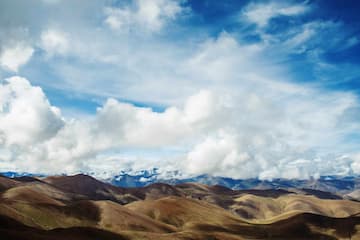 图片展示了高原地区的山脉和天空，白云在蓝天上漂浮。