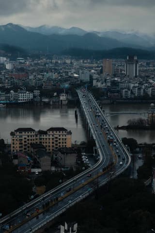 图片展示了城市景观，一条桥梁横跨水面，连接城市两岸，远处是山脉