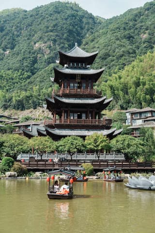 图片中，湖面上行驶着几艘小船，远处有一座多层宝塔建筑，背景是青山绿树。