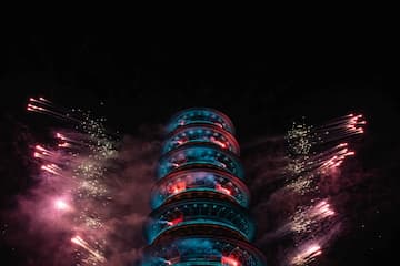 夜空中一座塔被灯光照亮，周围绽放着烟花。