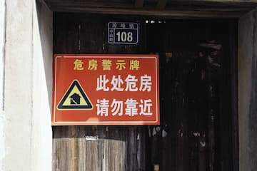 红色的危房警示牌贴在老旧的木门上 牌子上写着“此处危房请勿靠近”