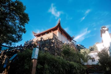 图片展示了一座位于山上的传统中式建筑，飞檐翘角，背景是蓝天白云。
