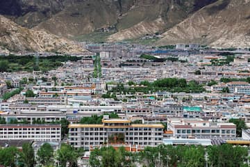 图片展示了拉萨的城市景观，建筑密集，背景是连绵的山脉。